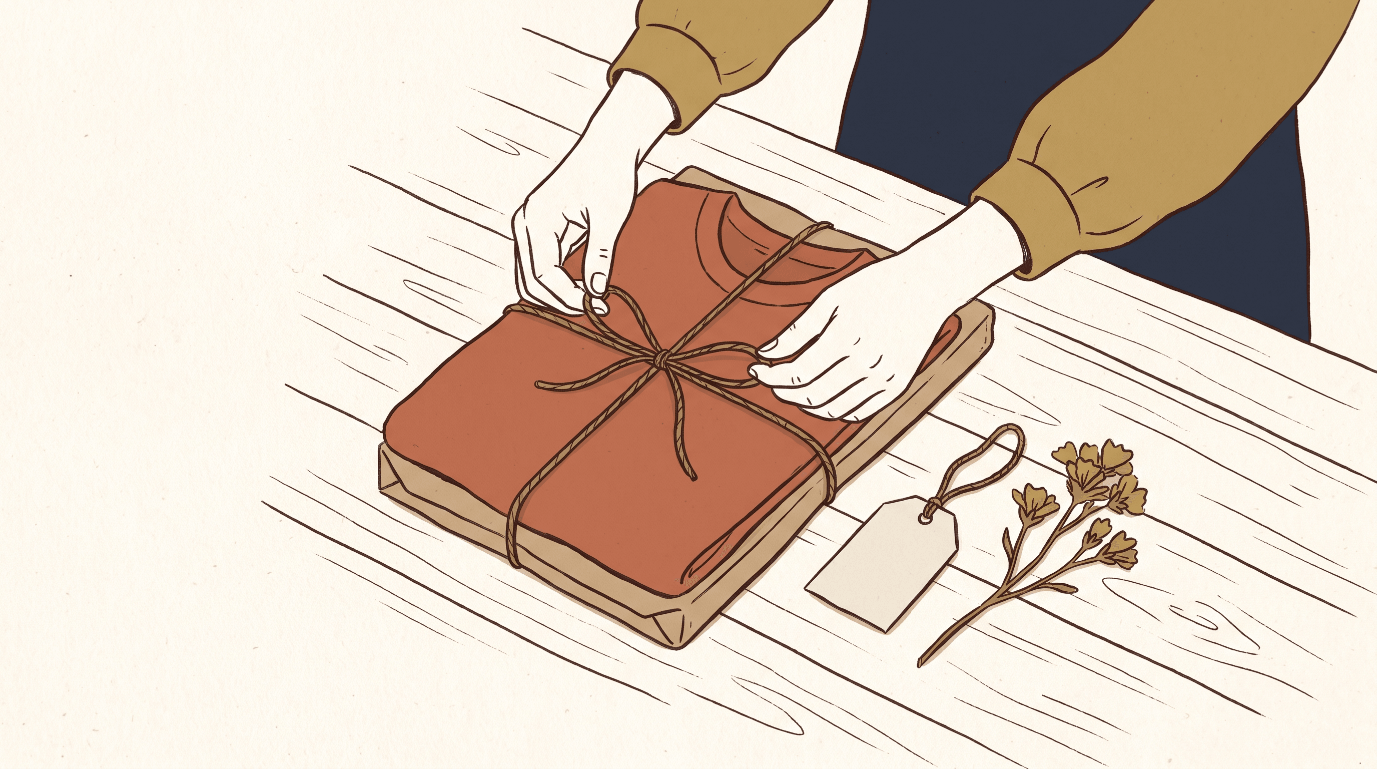 Two hands wrapping a folded t-shirt in kraft paper and twine with a small gift tag and a dried flower on a wooden table